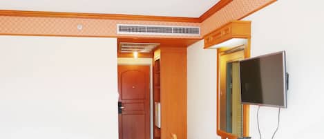 Een compacte kamer met een houten eettafel, twee stoelen, een aan de muur bevestigde televisie en een kitchenette met kastjes en een magnetron.