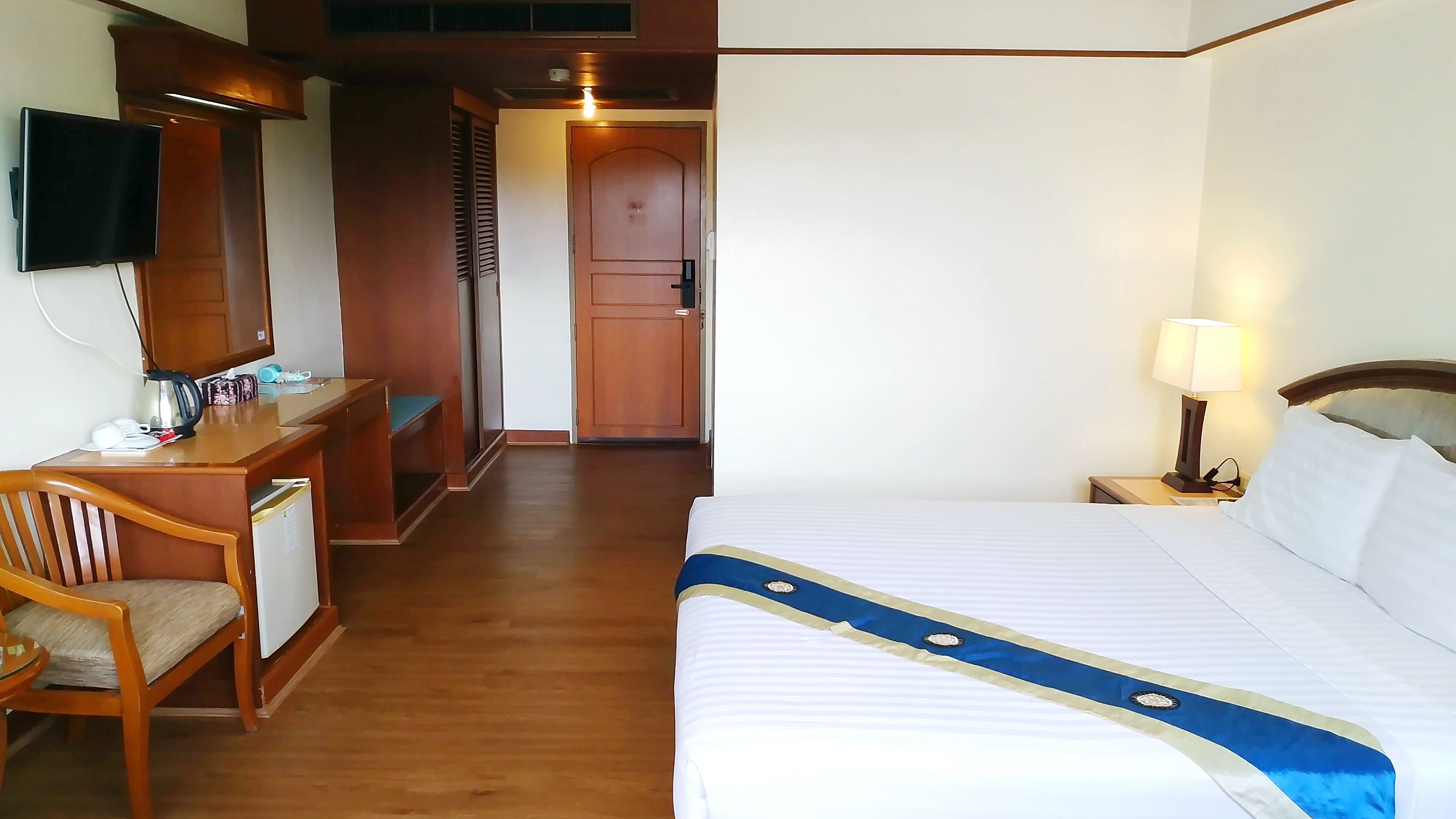 A hotel room with a bed, a desk with a chair, a television, and a door leading to another room.