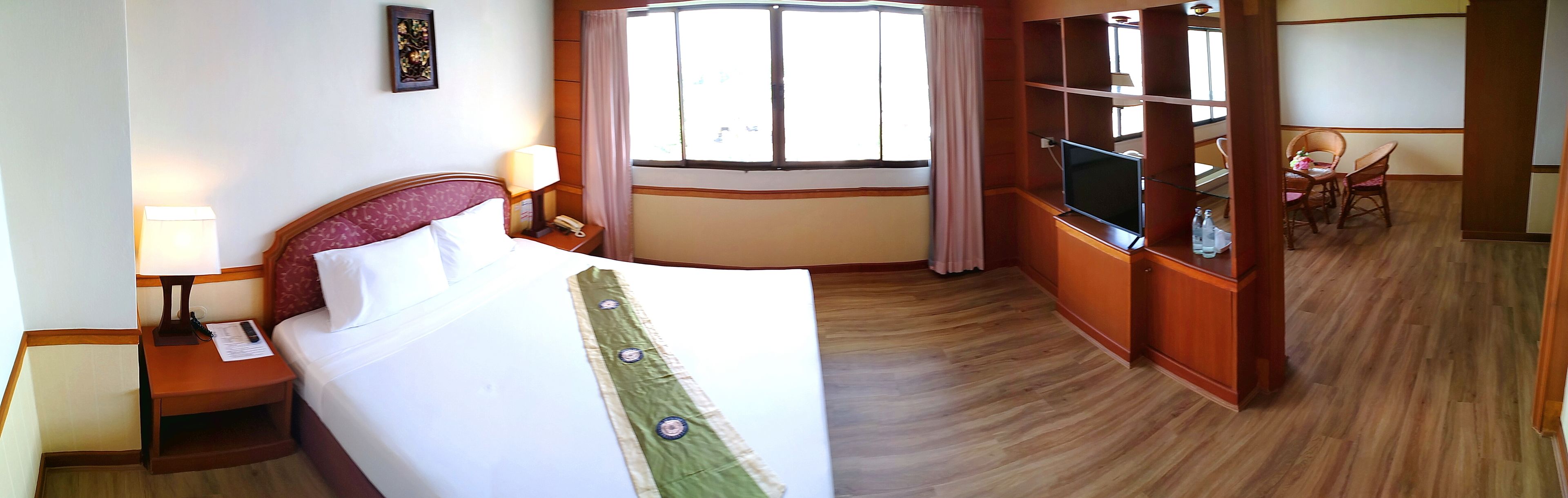 A hotel room with a bed, a desk with a lamp, a TV, and a dining area with chairs.