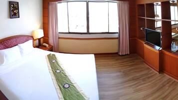 A hotel room with a bed, a desk with a lamp, a TV, and a dining area with chairs.