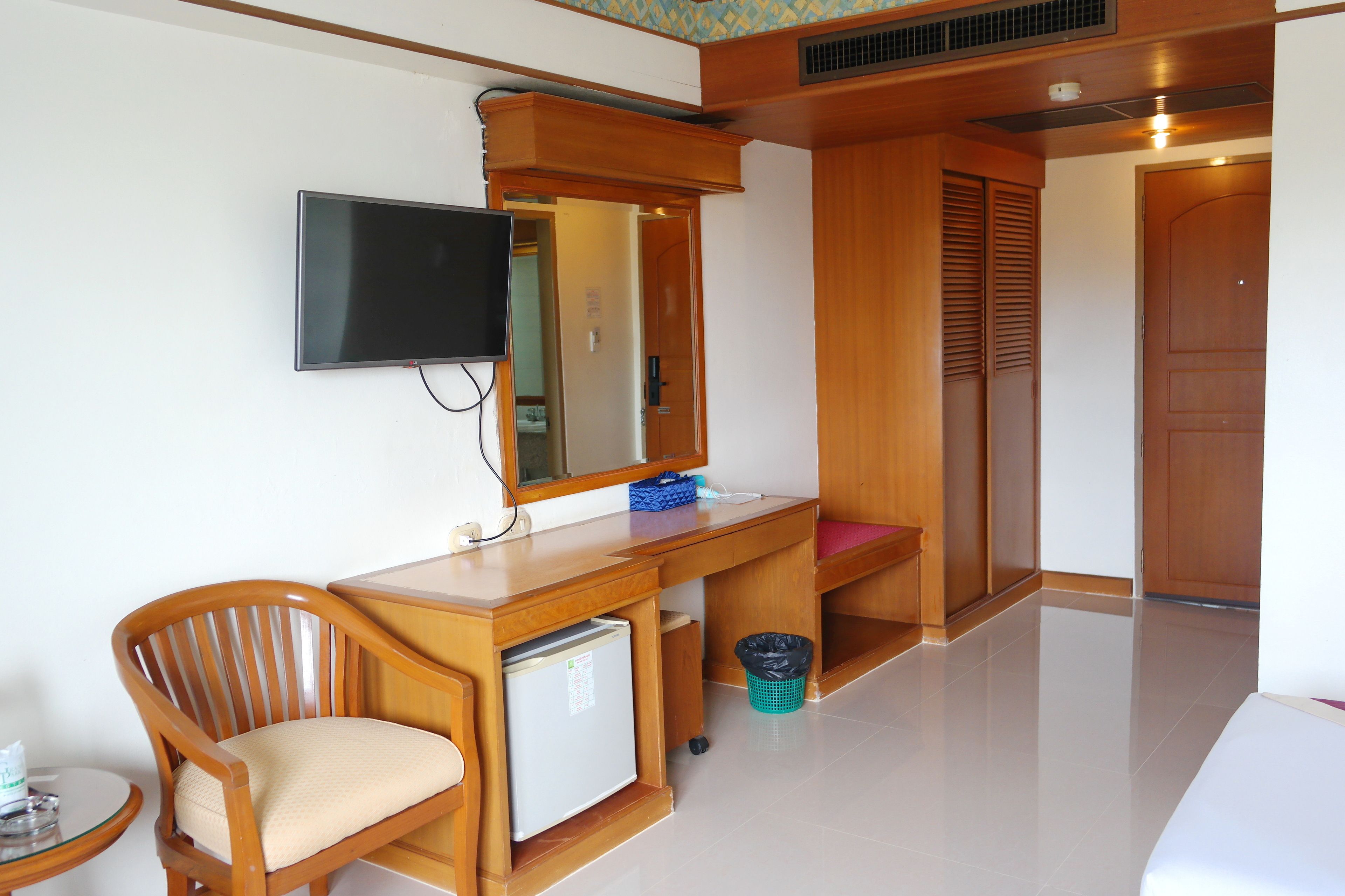 Ein Hotelzimmer mit Schreibtisch aus Holz, einem an der Wand befestigten Fernseher, einem kleinen Kühlschrank und einem Mülleimer.