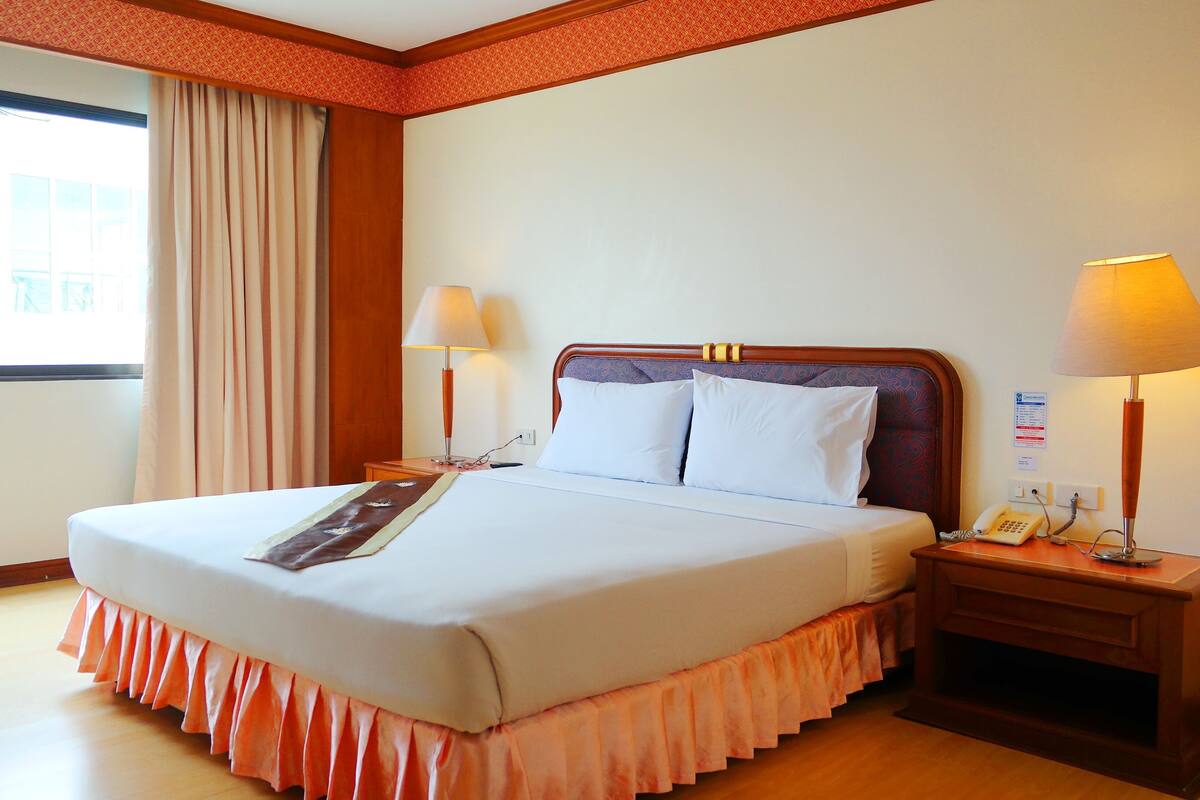 A hotel room with a large bed, two bedside lamps, a telephone, and a window with curtains.
