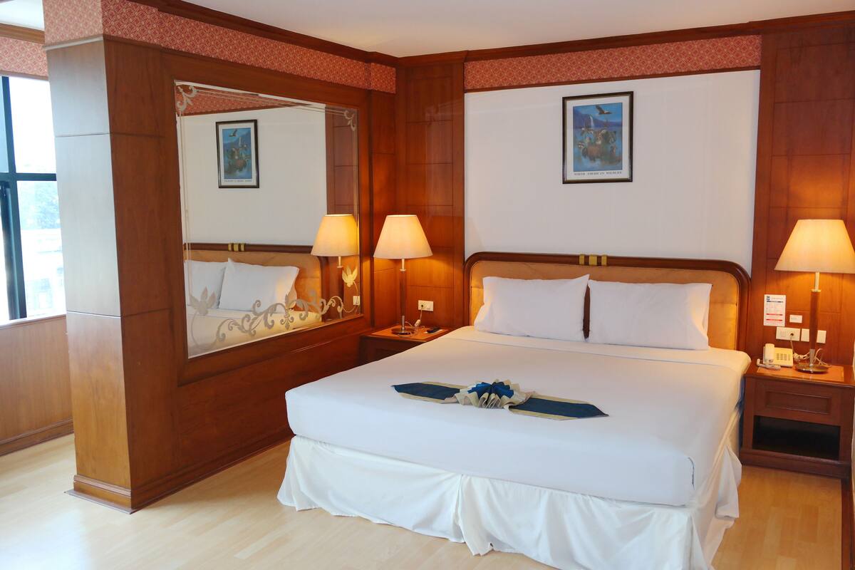A hotel room with a large bed, two bedside lamps, a nightstand, a mirror, and a framed picture on the wall.
