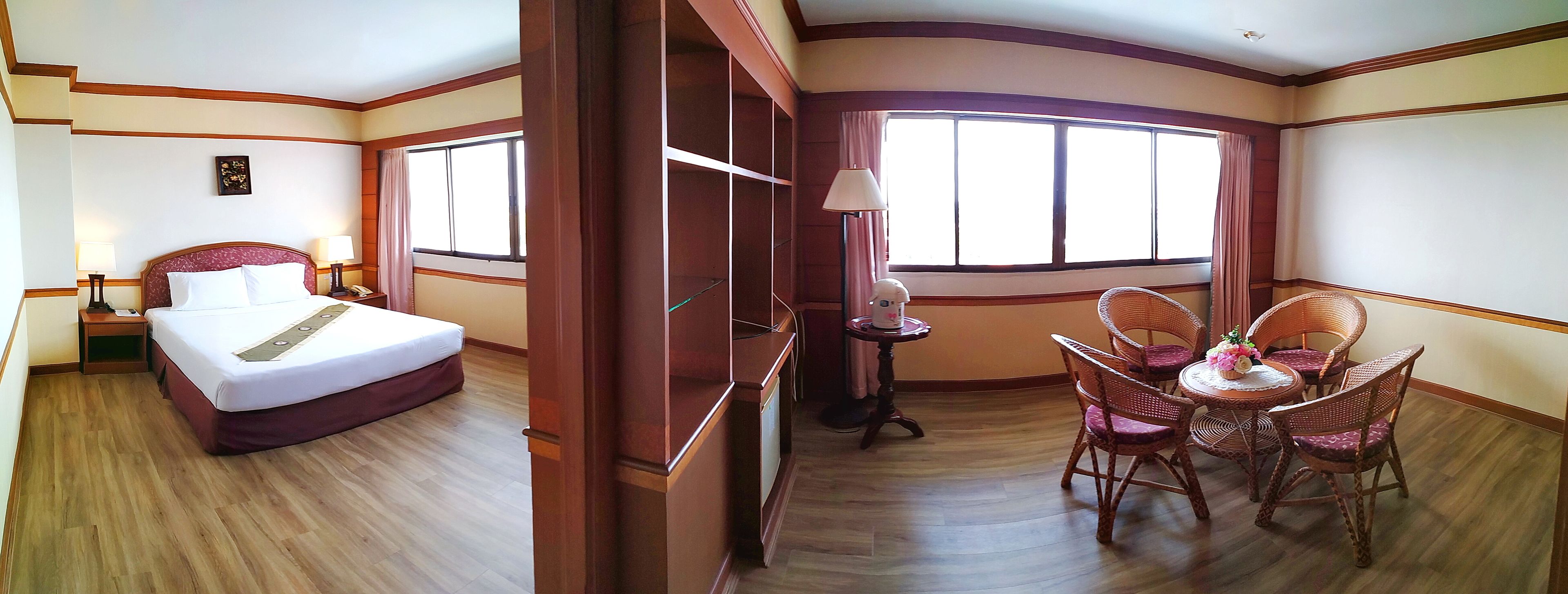 A hotel room with a bed, bedside table, lamp, and a dining area with wicker chairs and a table.