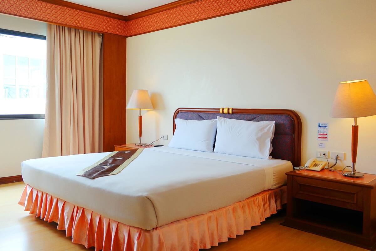 A hotel room with a large bed, two bedside lamps, a telephone, and a window with curtains.