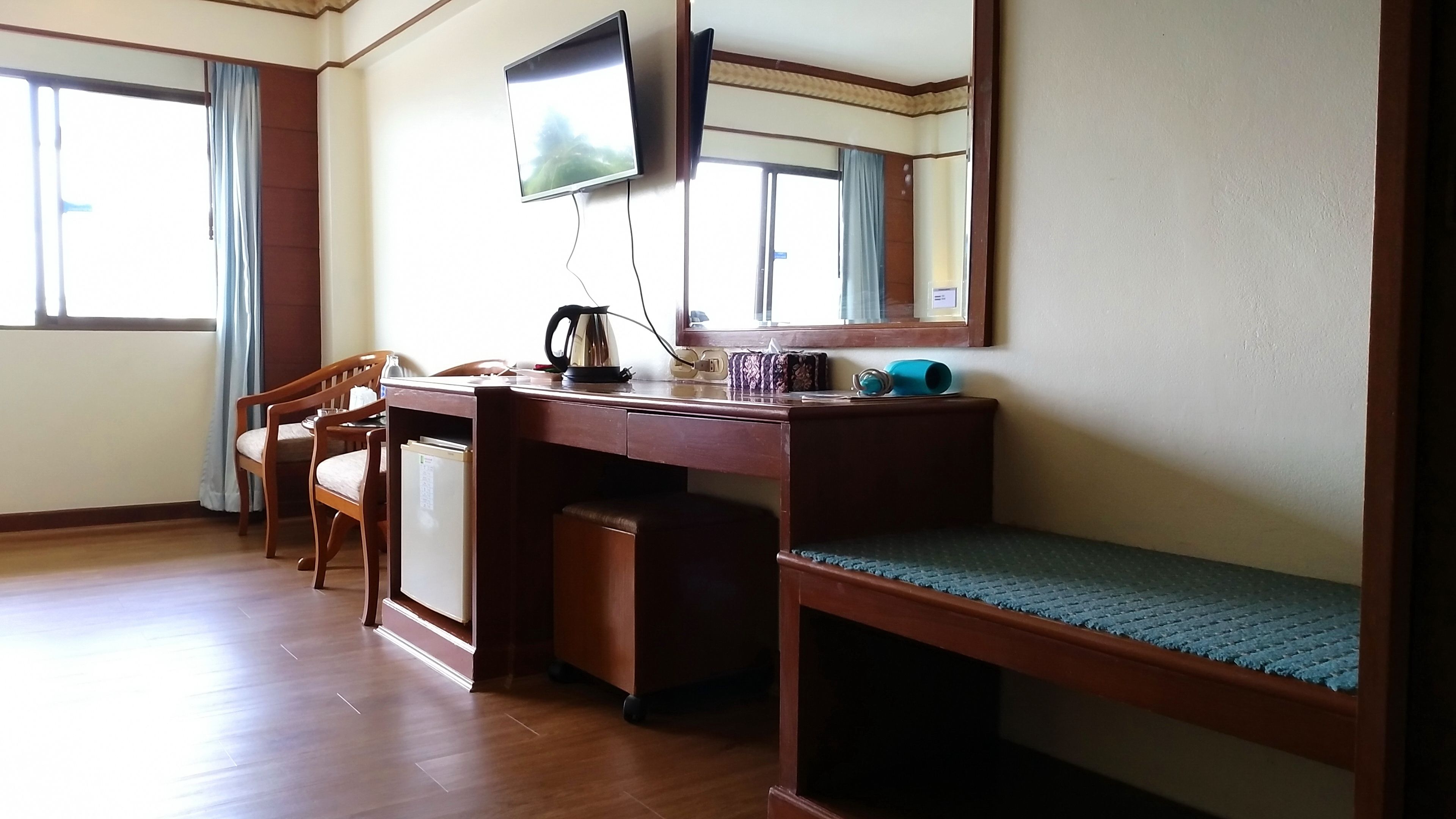 Habitación de hotel compacta con escritorio de madera, una silla, refrigerador pequeño, televisión montada en la pared y una ventana con cortinas.