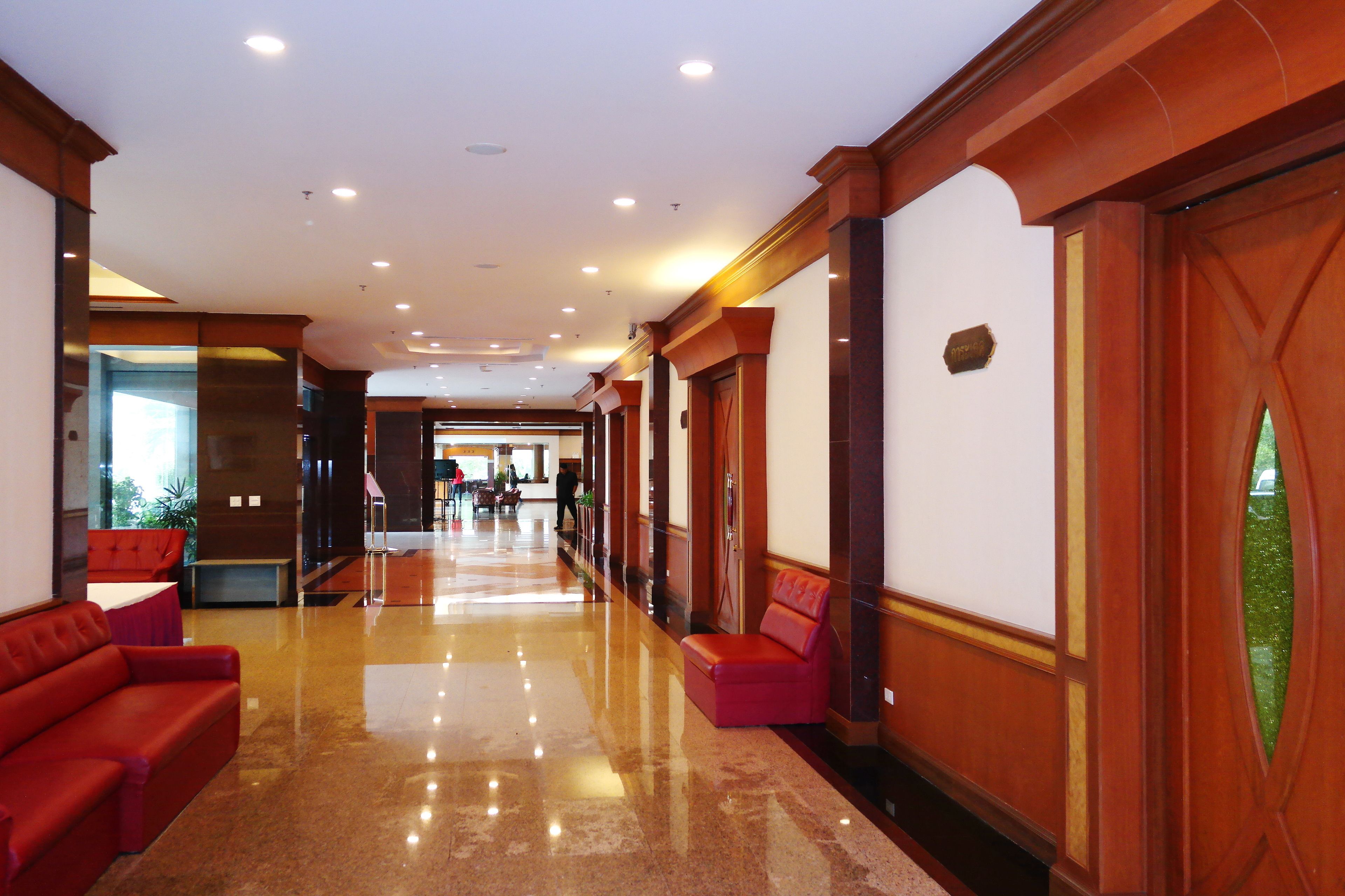 Un vestíbulo de hotel con piso pulido, asientos rojos y paneles de madera.