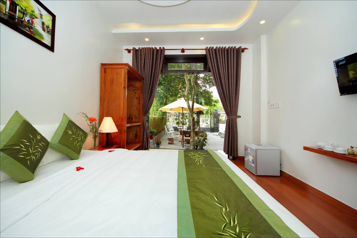 Ein Hotelzimmer mit Bett, Fernseher, kleinem Kühlschrank und Blick auf die Außenpatio-Terrasse.