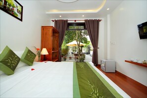A hotel room with a bed, a TV, a small refrigerator, and a view of the outdoor patio area.