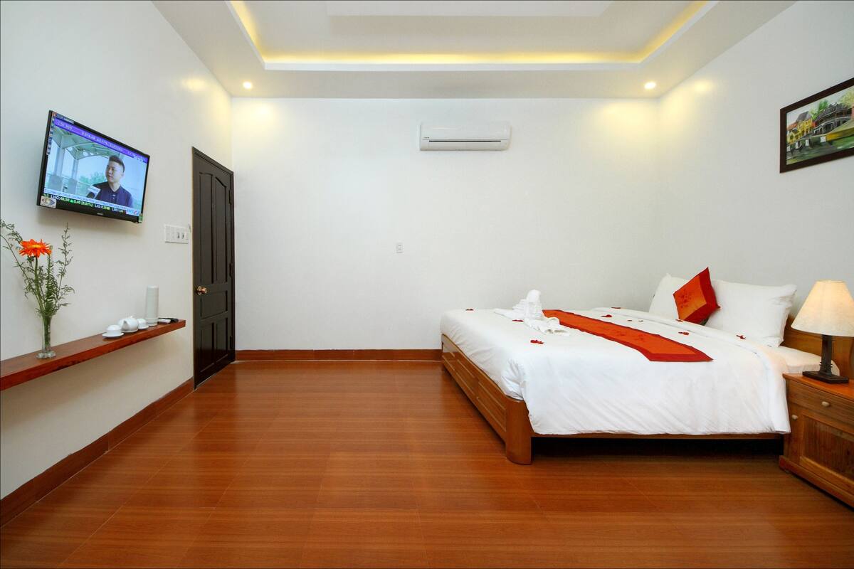 Ein Hotelzimmer mit einem Bett, einem an der Wand befestigten Fernseher, einem Regal mit Dekoration und einem Holzboden.