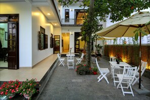 A courtyard with white furniture, a large umbrella, and potted plants.