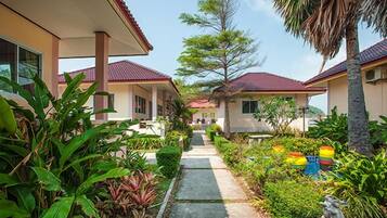 Un sendero que conduce a una hilera de casas con tejados rojos, rodeado de exuberante vegetación y una estatua.