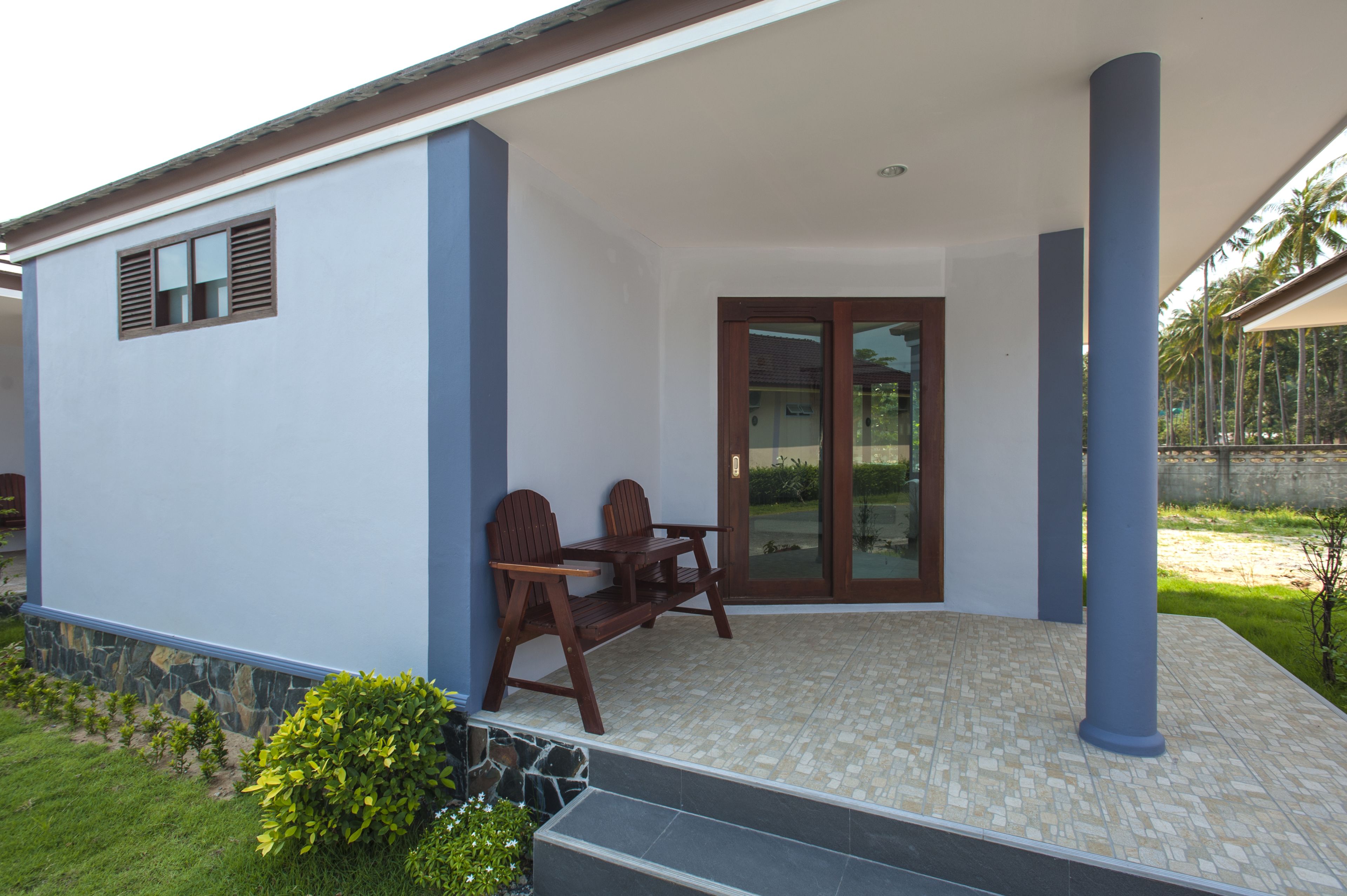 A covered patio area with a table and chairs, a stone wall, and a glass door leading to a garden.