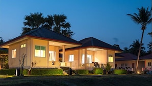 Una casa de dos pisos con un porche cubierto e iluminación exterior al anochecer.