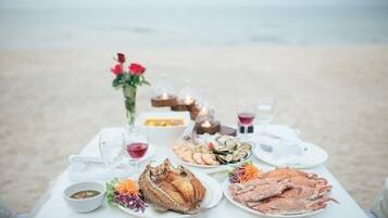 A table set on a beach with seafood dishes, glasses, and a vase with flowers.