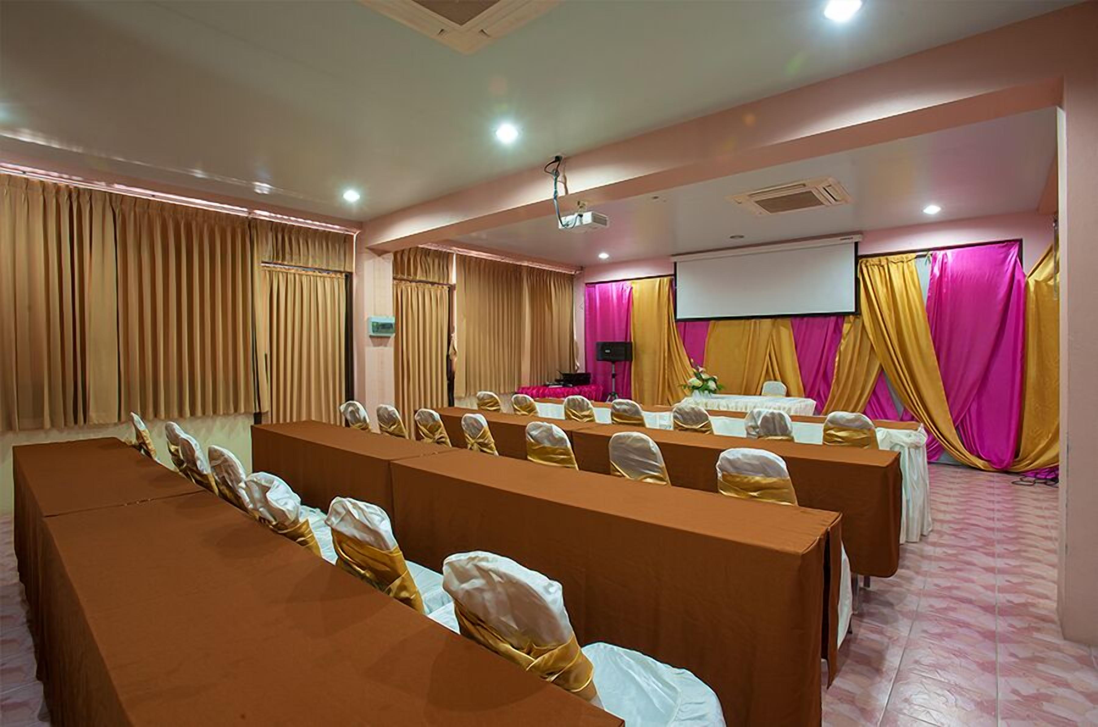 A conference room with long tables, chairs, a projector screen, and a stage.