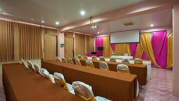 A conference room with long tables, chairs, a projector screen, and a stage.