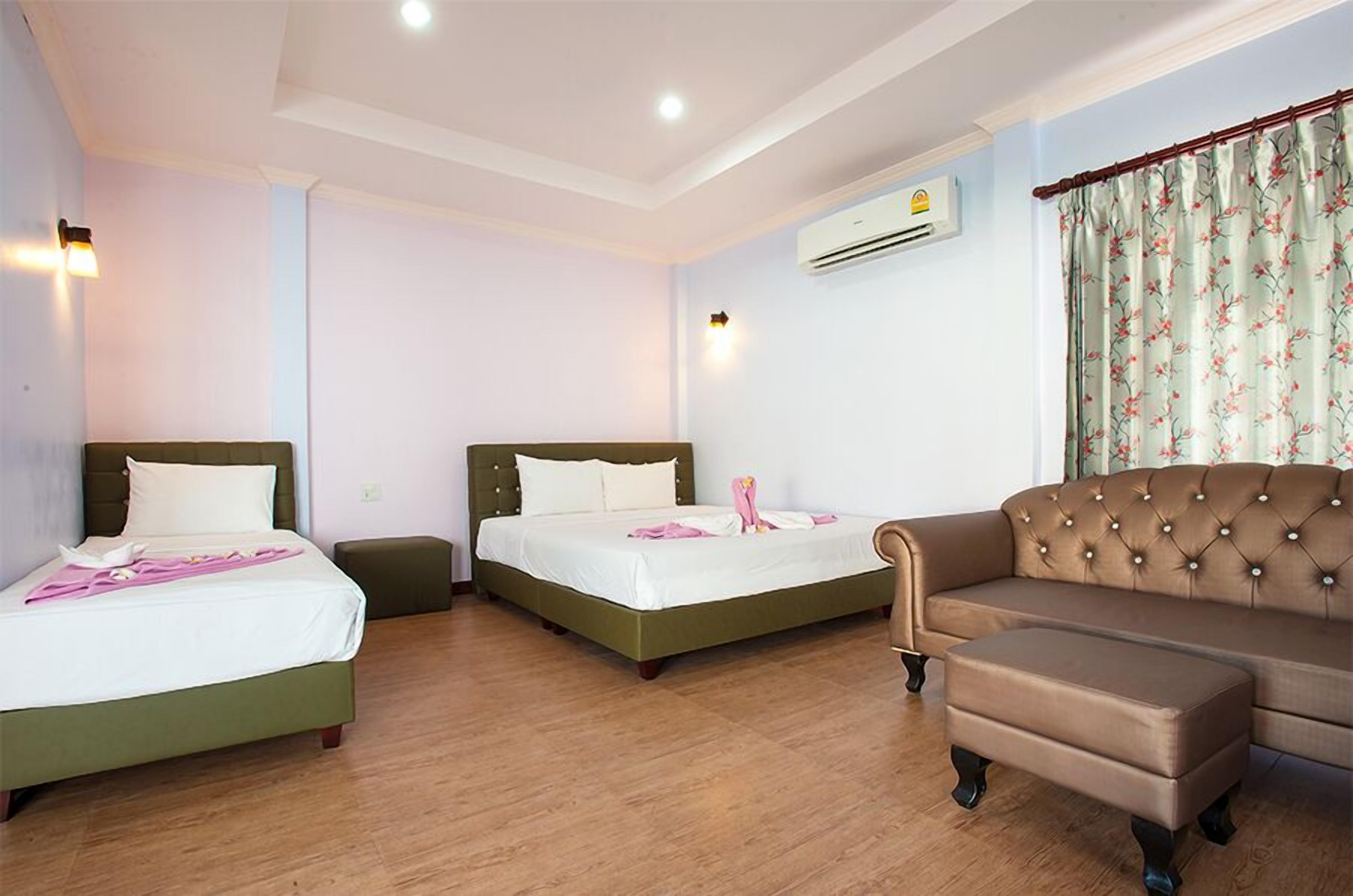 A hotel room with two beds, a sofa, and an air conditioning unit.
