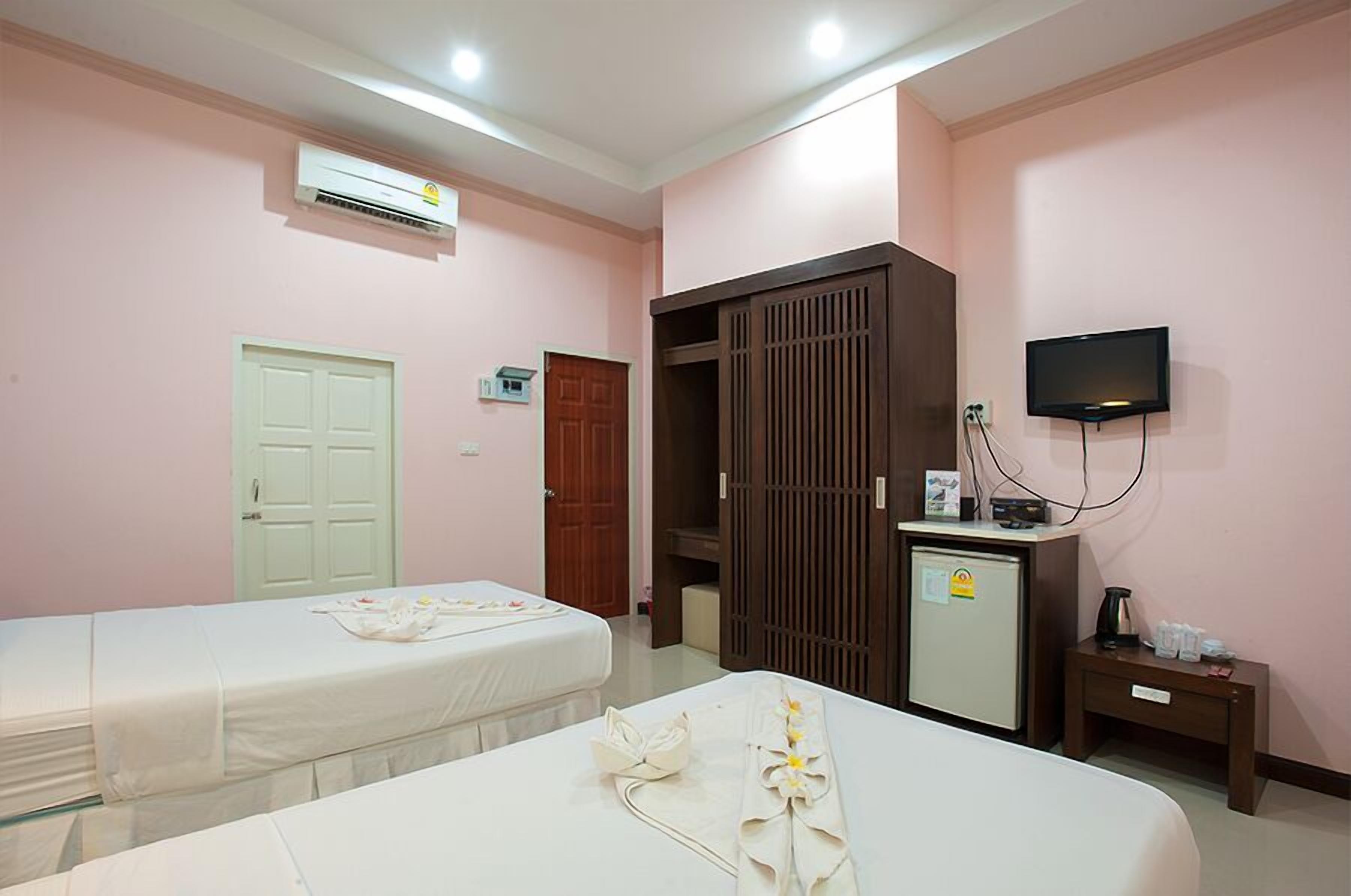 A hotel room with two beds, a wardrobe, a desk with a television, and an air conditioning unit.