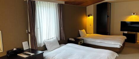 Une chambre d’hôtel avec deux lits, un bureau, un téléphone, une télévision et un ventilateur de plafond.