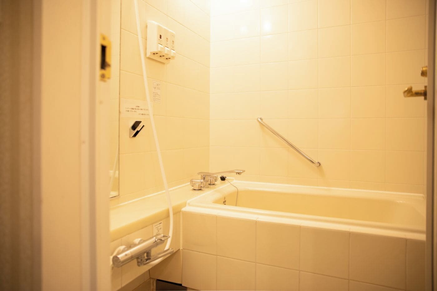 A bathroom with a bathtub, a handrail, and a wall-mounted electrical outlet.