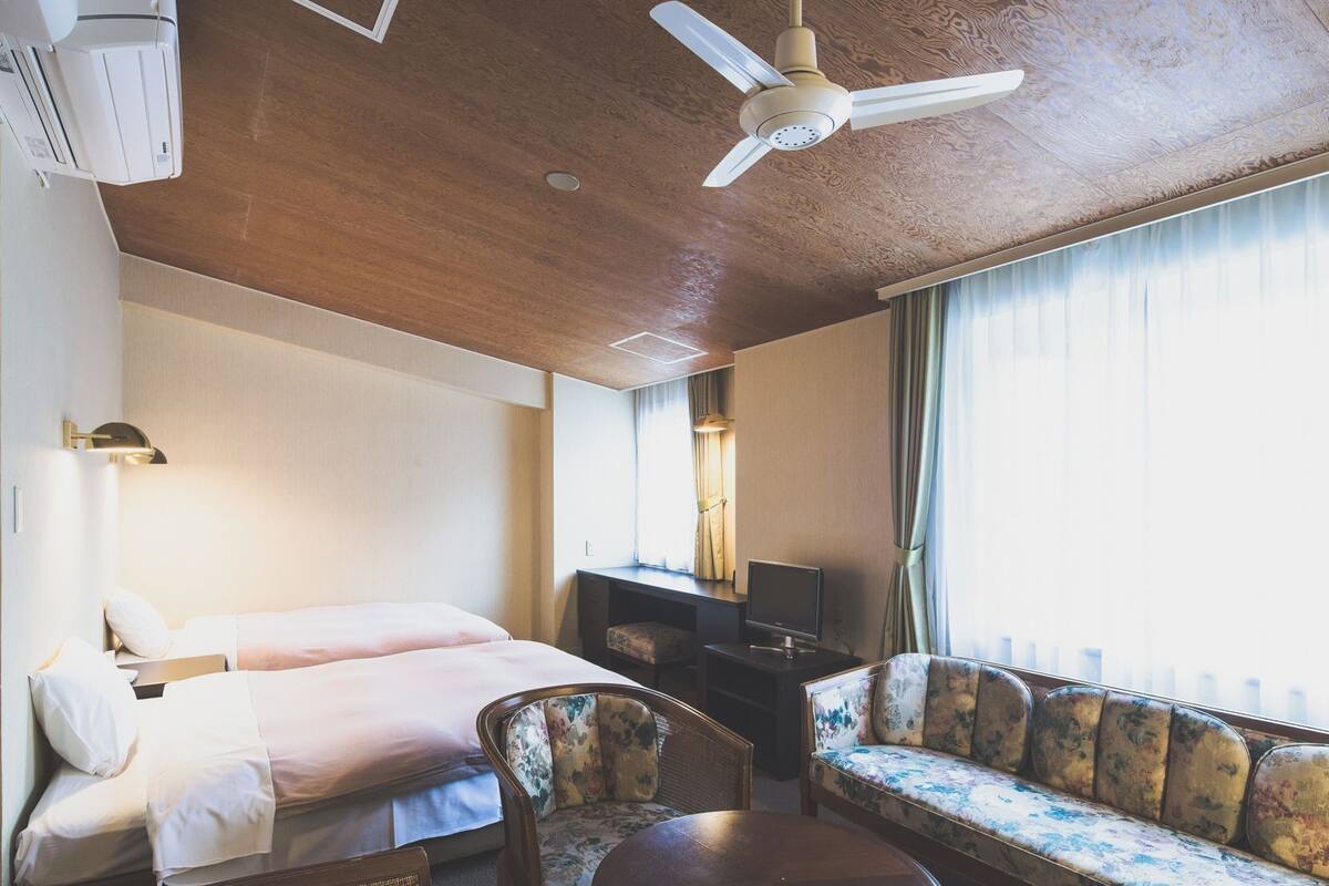 Une chambre d’hôtel comprenant un lit, un bureau, un canapé, une chaise, une table ronde et un ventilateur de plafond.