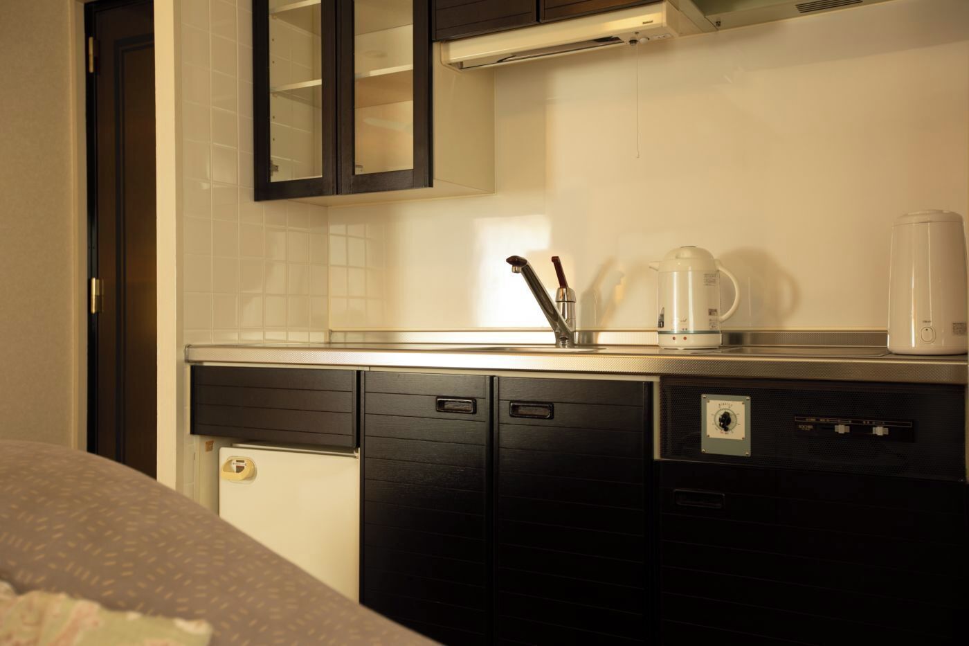 A compact kitchen with a sink, a coffee maker, and a kettle on the counter.