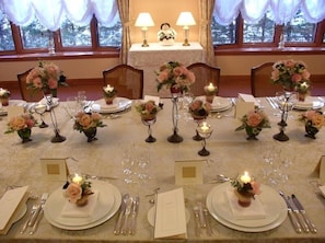 Une table à manger dressée pour un repas formel, agrémentée de compositions florales, de bougies et offrant une vue sur un paysage enneigé par de grandes fenêtres.