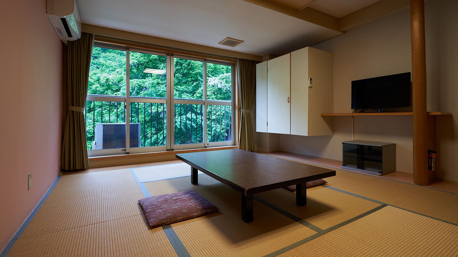 A tatami mat room with a low table, a cushion, a television, and a cabinet.