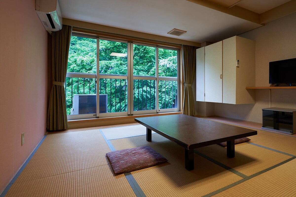 A tatami mat room with a low table, a cushion, a television, and a cabinet.