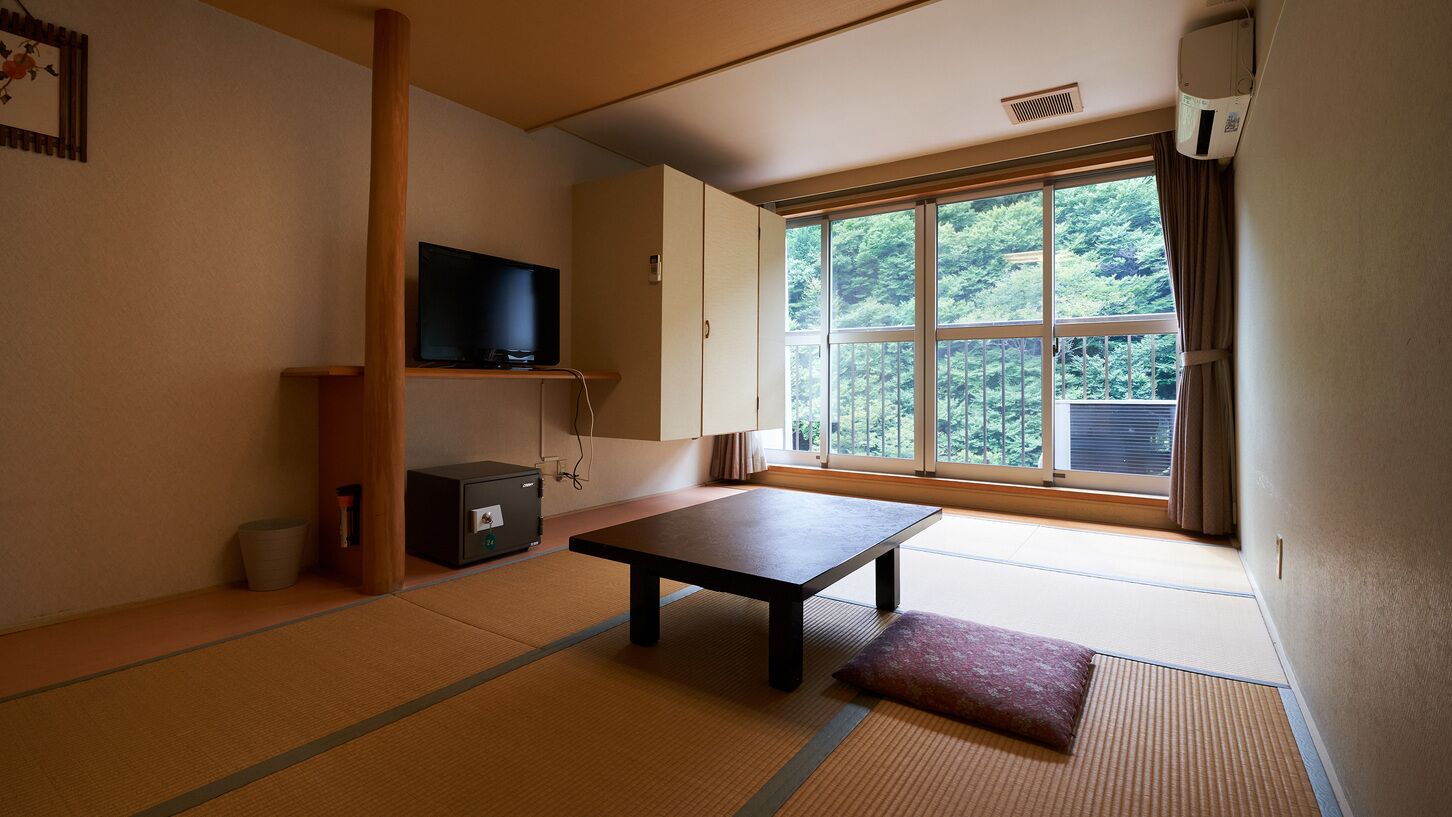 A traditional Japanese room with tatami flooring, a television, a cabinet, and a window with a view of trees.