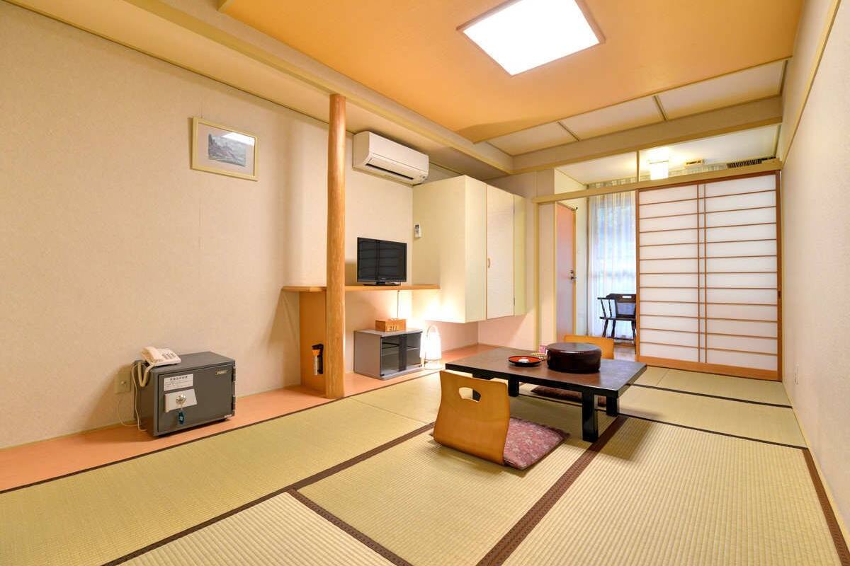 A traditional Japanese room with tatami flooring, a low table with cushions, a television, and a sliding door.