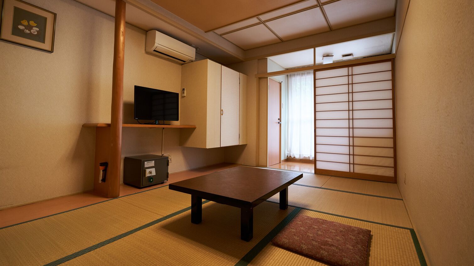 A traditional Japanese room with tatami flooring, a low table, a television, and sliding doors.