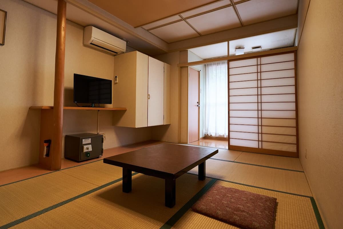 A traditional Japanese room with tatami flooring, a low table, a television, and sliding doors.