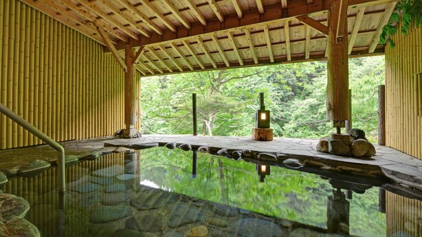 A serene hot spring area with a wooden deck, stone steps, and a view of lush greenery.