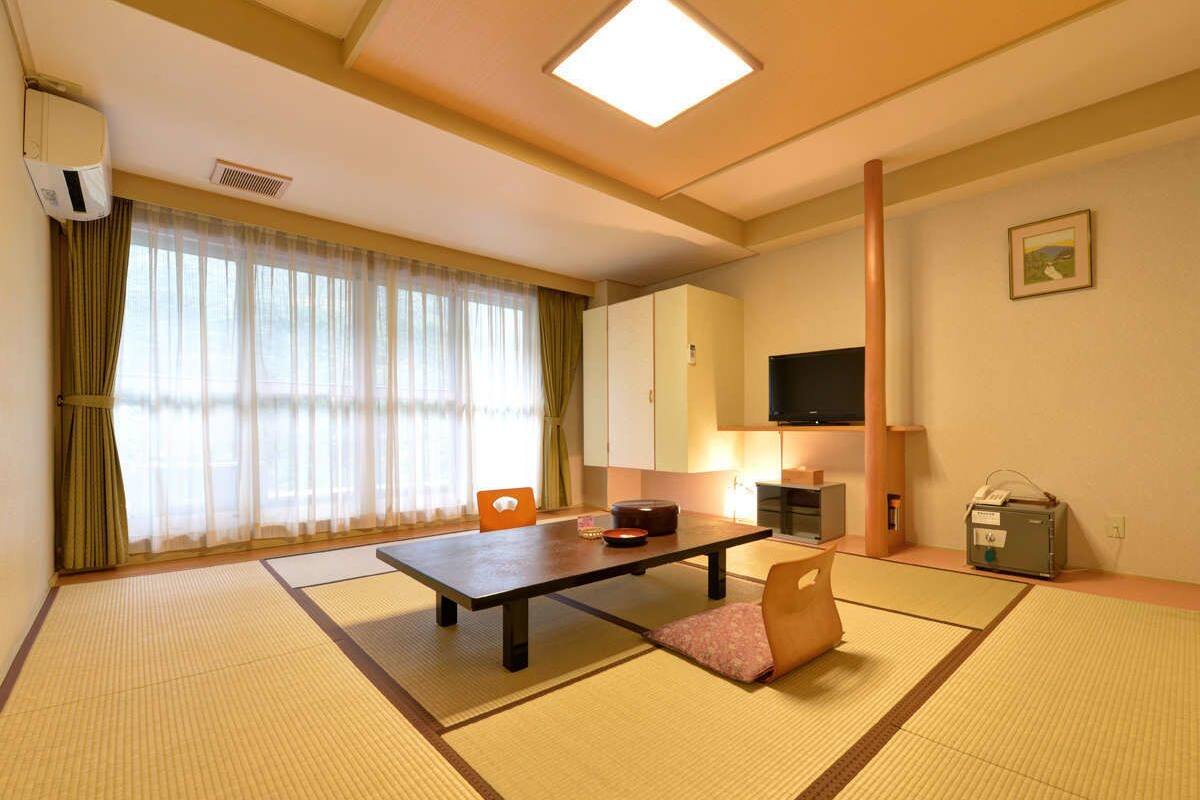 A traditional Japanese room with tatami flooring, a low table, a cushioned chair, a television, and a small cabinet.