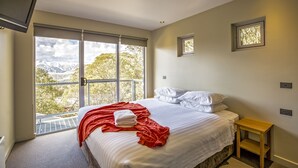 A bedroom with a large window, a bed with white linens, a red blanket, and a small wooden nightstand.