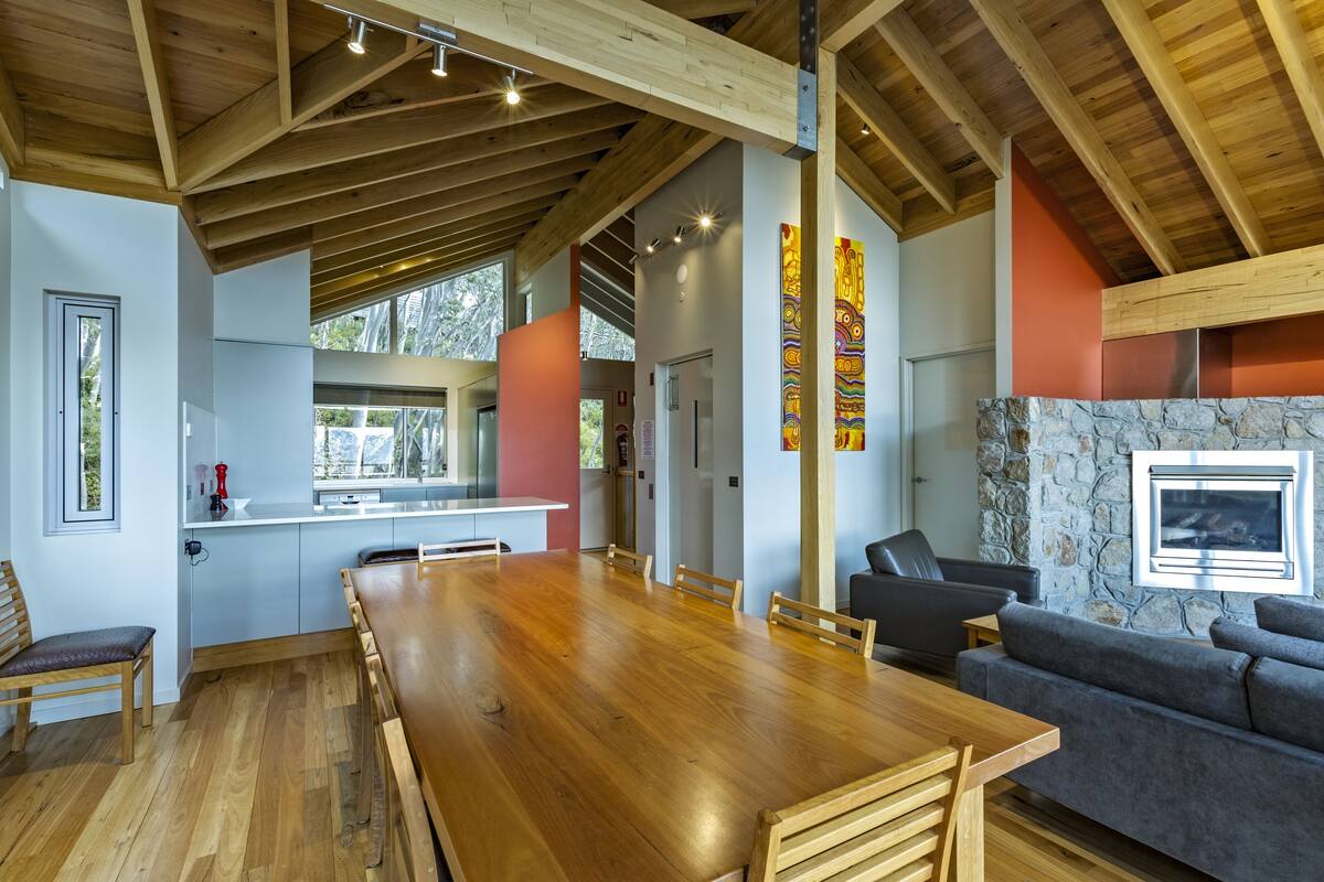 A spacious kitchen with a long wooden table, a stone fireplace, and a modern grey sofa.