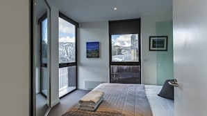 A modern bedroom with a large bed, a view of a snowy landscape, and a cityscape through the window.