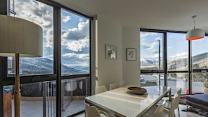 A modern dining area with a large table and chairs, large windows offering a mountain view, and a hanging light fixture.