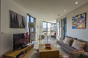 A modern living room with a flat-screen TV, a wooden coffee table, and a sofa with decorative pillows. - Altezza 1570 (Falls Creek)