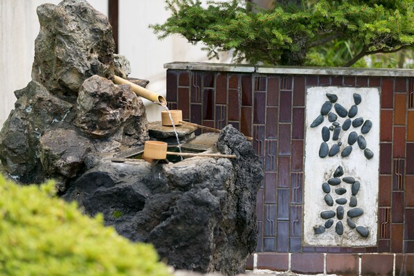 Um jardim de pedras com um elemento aquático tradicional japonês, um rastelo de madeira e uma bacia de pedra.