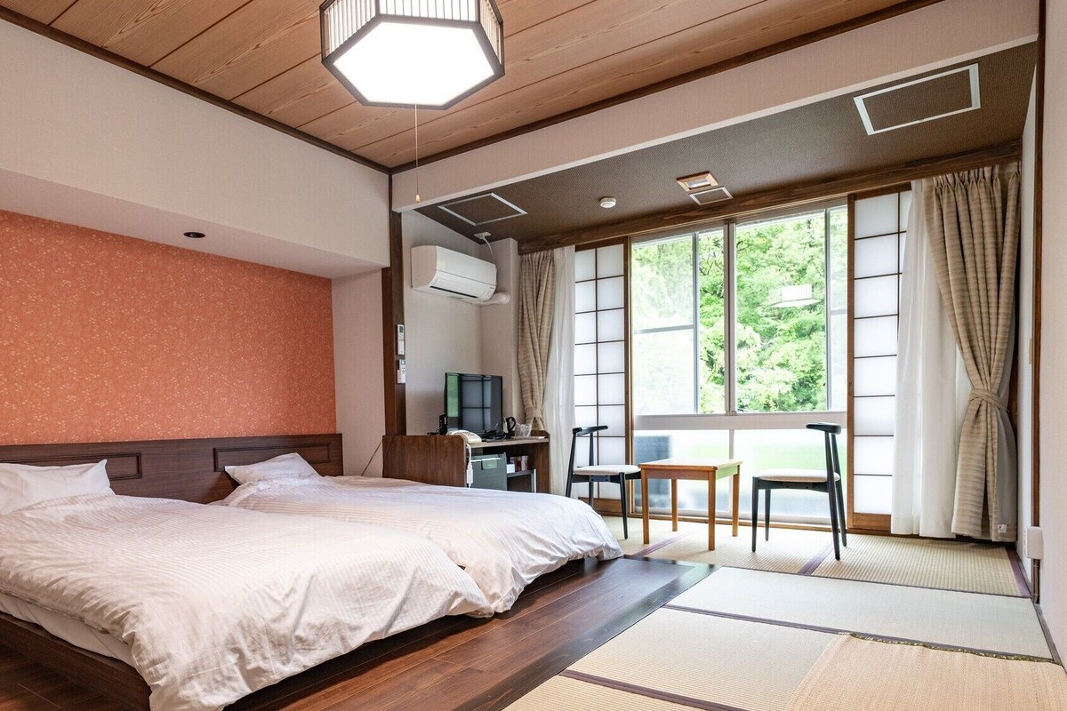 A hotel room with a bed, a desk, a chair, and a large window with curtains.