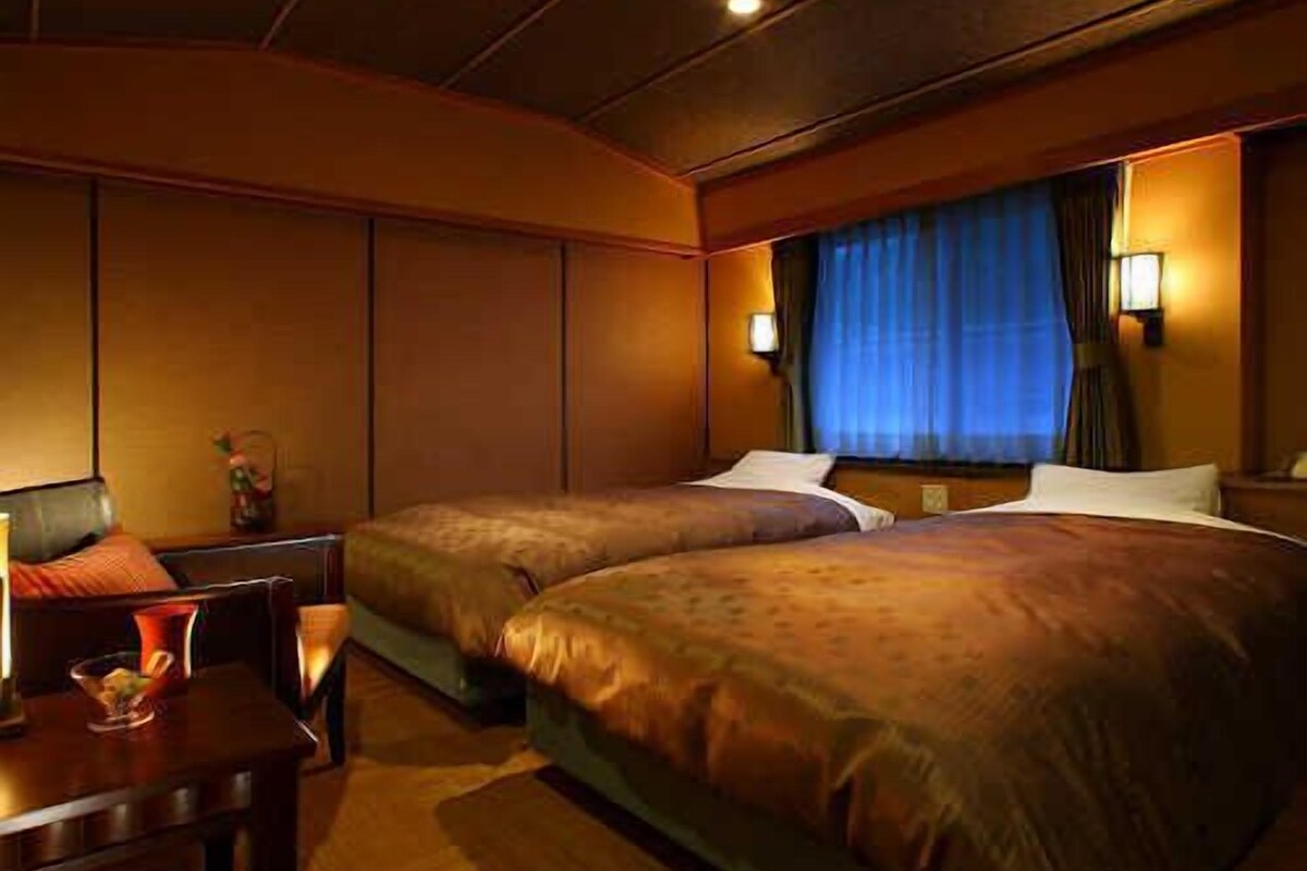 A hotel room with two beds, a desk, and a window with curtains.