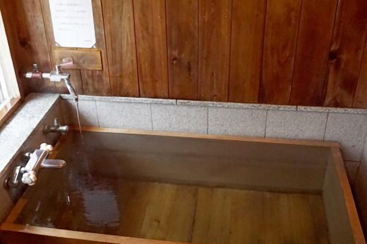 A wooden bathtub with faucets, a wooden wall, and a tiled floor.