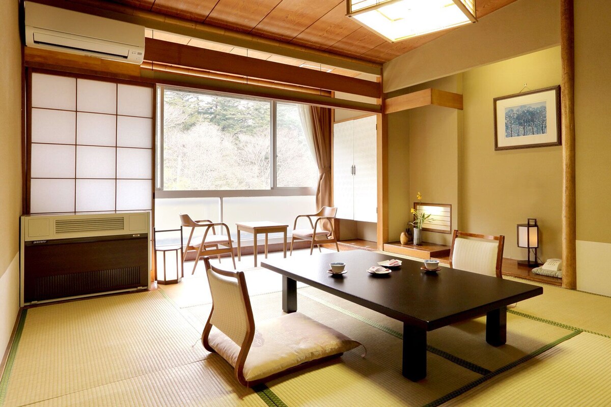 A traditional Japanese room with tatami flooring, a low table, chairs, and sliding doors.