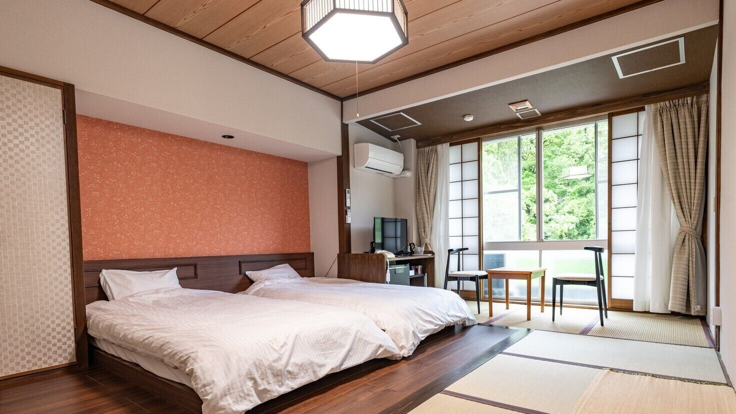 Ein Hotelzimmer mit einem großen Bett, einem Schreibtisch und Blick auf Grün hinter den Fenstern.
