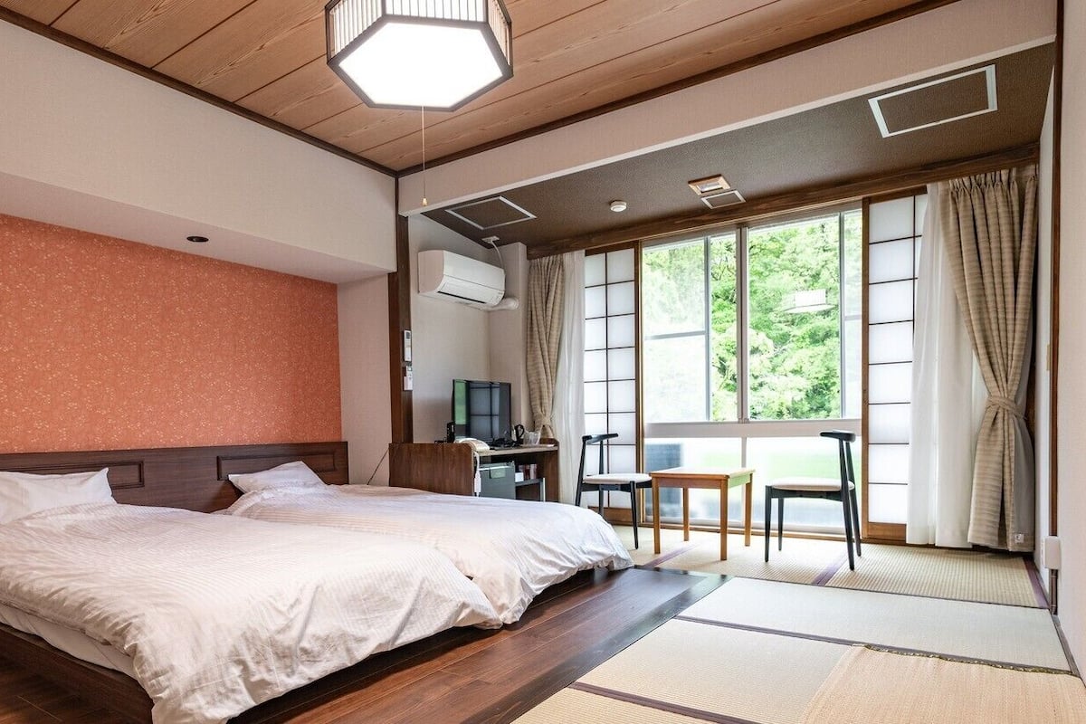 Habitación de hotel con una cama grande, un escritorio y vistas a zonas verdes por las ventanas.