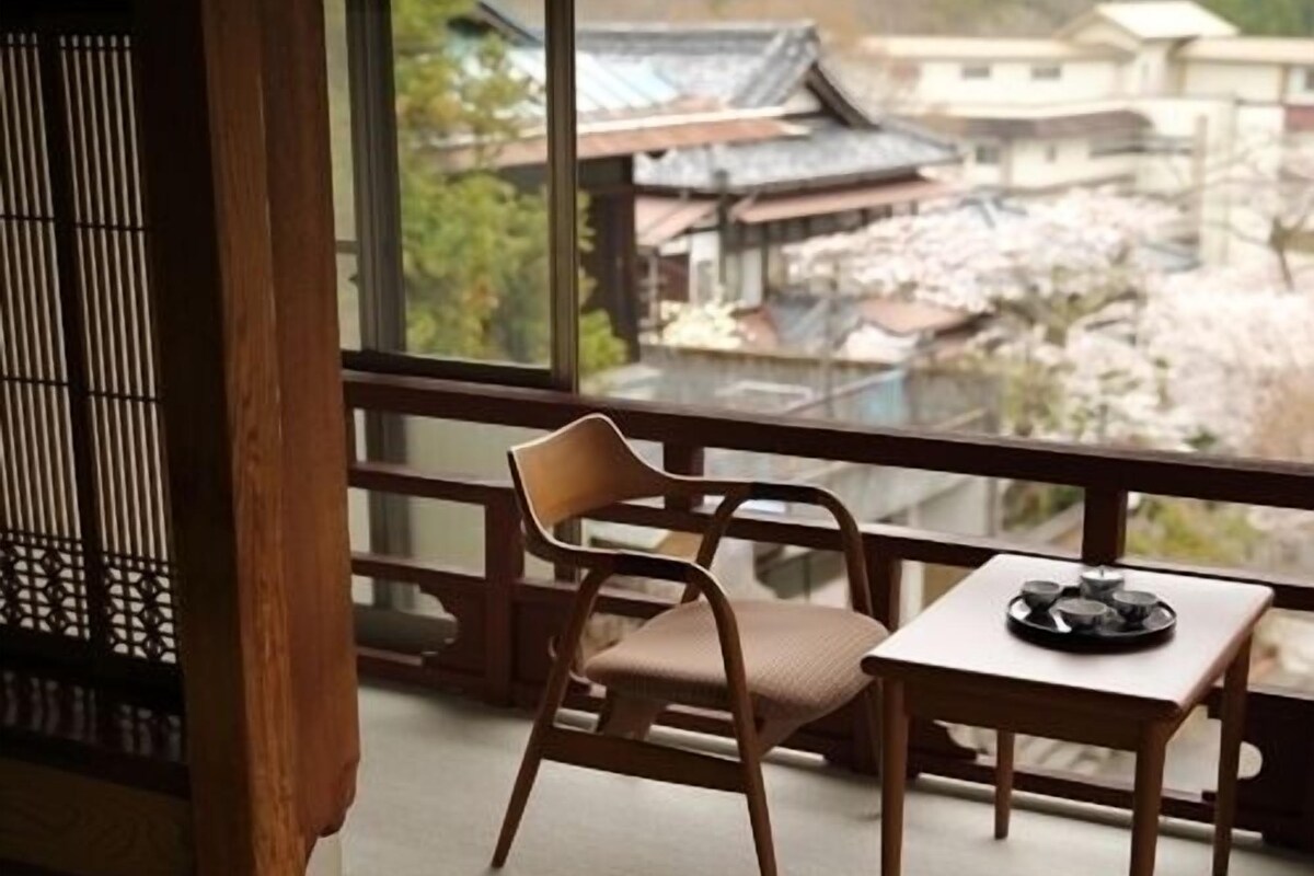 A room with a traditional Japanese style, featuring tatami flooring, a low table with a vinyl mat, and a chair.
