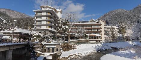 A multi-story hotel with a modern architectural design, located near a river with snow-covered surroundings.
